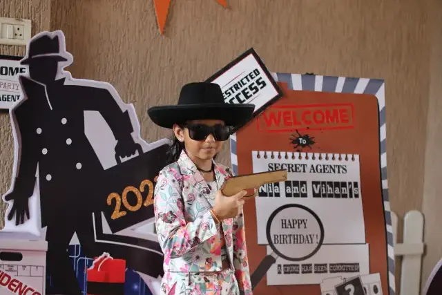 A child in a black hat and dark glasses posing in front of a Secret Agents spy-themed birthday backdrop