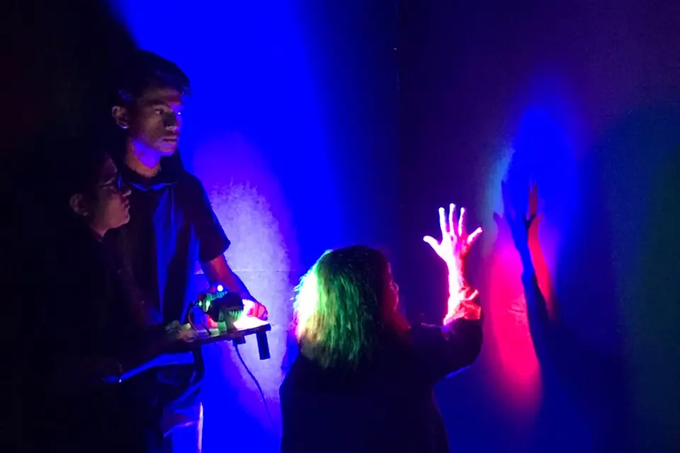 A child silhouetted with glowing hands raised in a darkened room lit blue and magenta