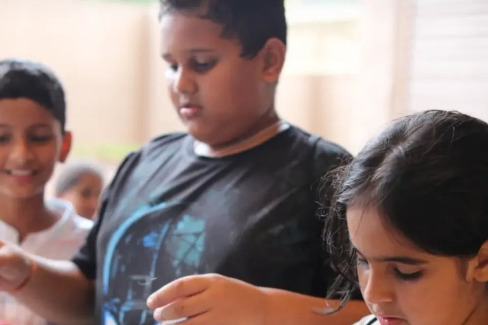 Two children assembling a small wooden model kit at a table, concentrating on the parts in their hands
