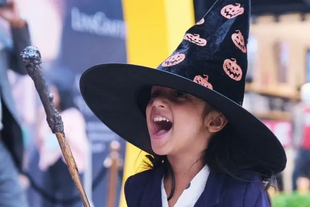 A girl in a witch’s hat laughing as she holds up a wand at a Science of Wizards party