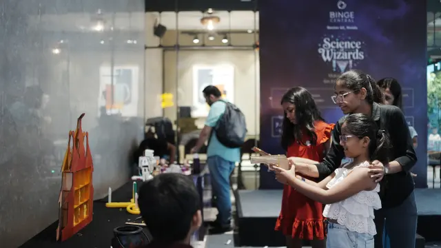 A mother steadying her daughter’s aim at a wooden castle target game during a MakerMasti family day