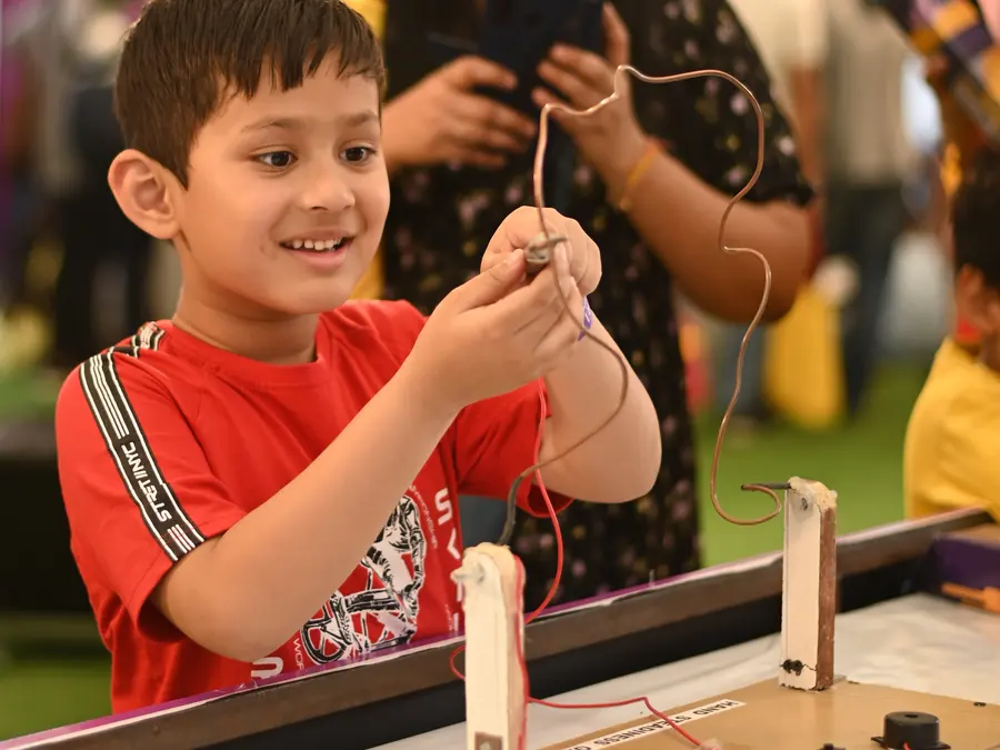 A boy grinning as he lifts a wire loop off a buzzing circuit he has just built at a MakerMasti party