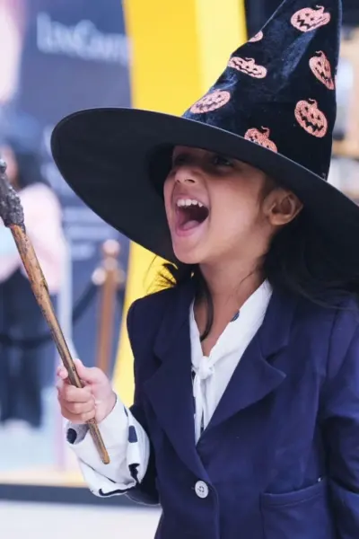 A girl in a witch hat laughing as she raises a light-up wand